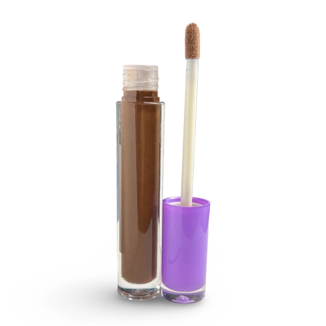 A clear cylindrical cosmetic tube filled with medium brown liquid, shown next to its purple cap and applicator wand on a white background.