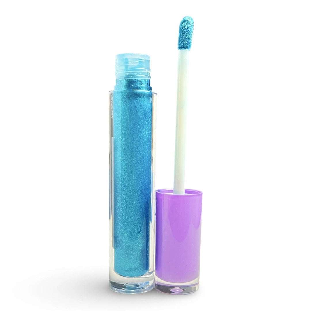 A tube of glittery blue lip gloss or liquid shimmer, shown open with the cap removed and the applicator wand standing beside it. The product container is clear, revealing the sparkling blue formula inside, while the cap is a glossy lavender purple.