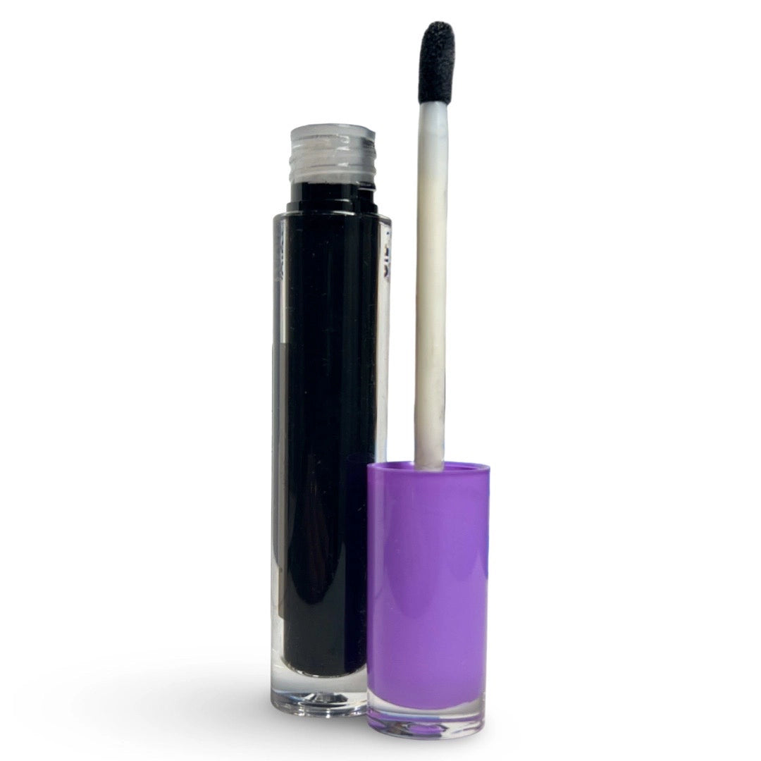 A clear cylindrical cosmetic tube filled with black product stands next to its purple cap, with a white-handled applicator wand resting inside the cap, on a white background.